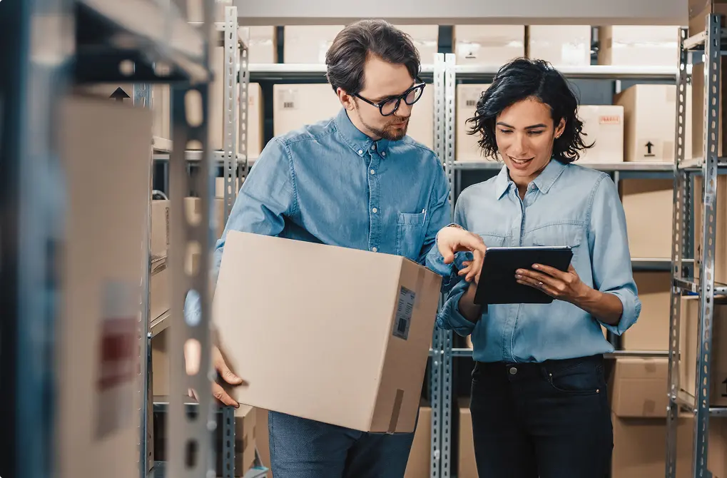 Two people looking at a tablet with boxes in the background
